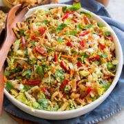 Large serving bowl full of Chinese chicken salad with cabbage, peanuts, sesame seeds, wonton strips, bell peppers.