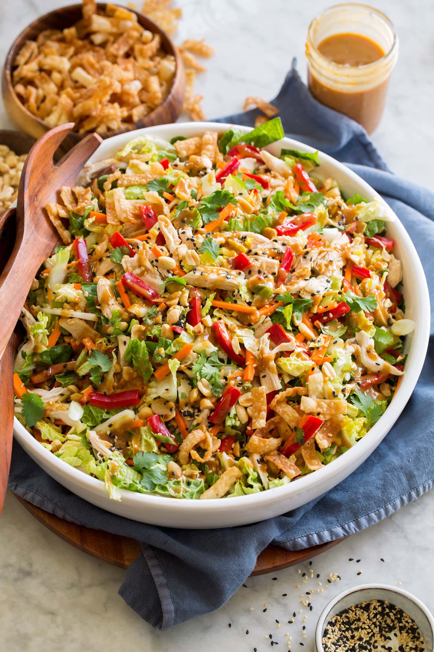 Large serving bowl full of Chinese chicken salad with cabbage, peanuts, sesame seeds, wonton strips, bell peppers.