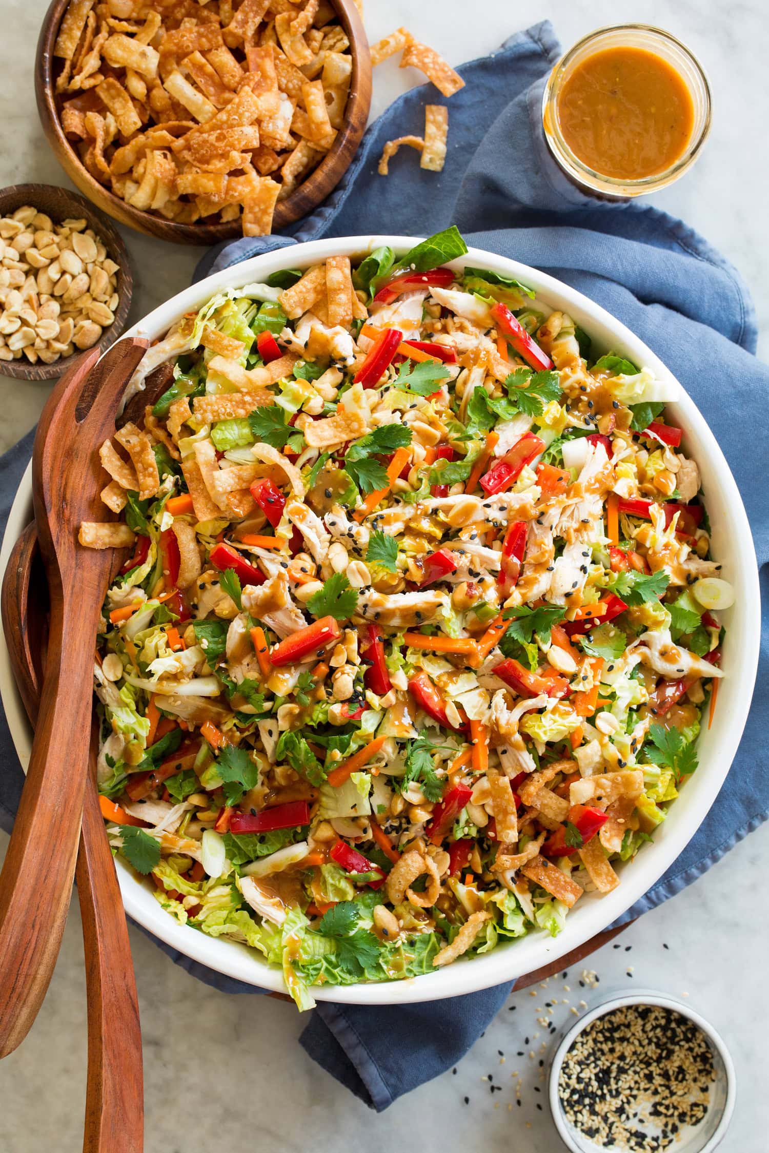 Overhead photo of Chinese chicken salad in a large white salad bowl with a blue cloth underneath. It's set on a marble surface.