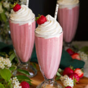 Three homemade strawberry milkshakes in tall glasses topped with whipped cream and strawberries.