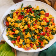 Tofu scramble in a white ceramic bowl over a marble surface with a green cloth to the side.