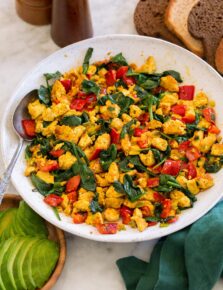 Tofu scramble in a white ceramic bowl over a marble surface with a green cloth to the side.