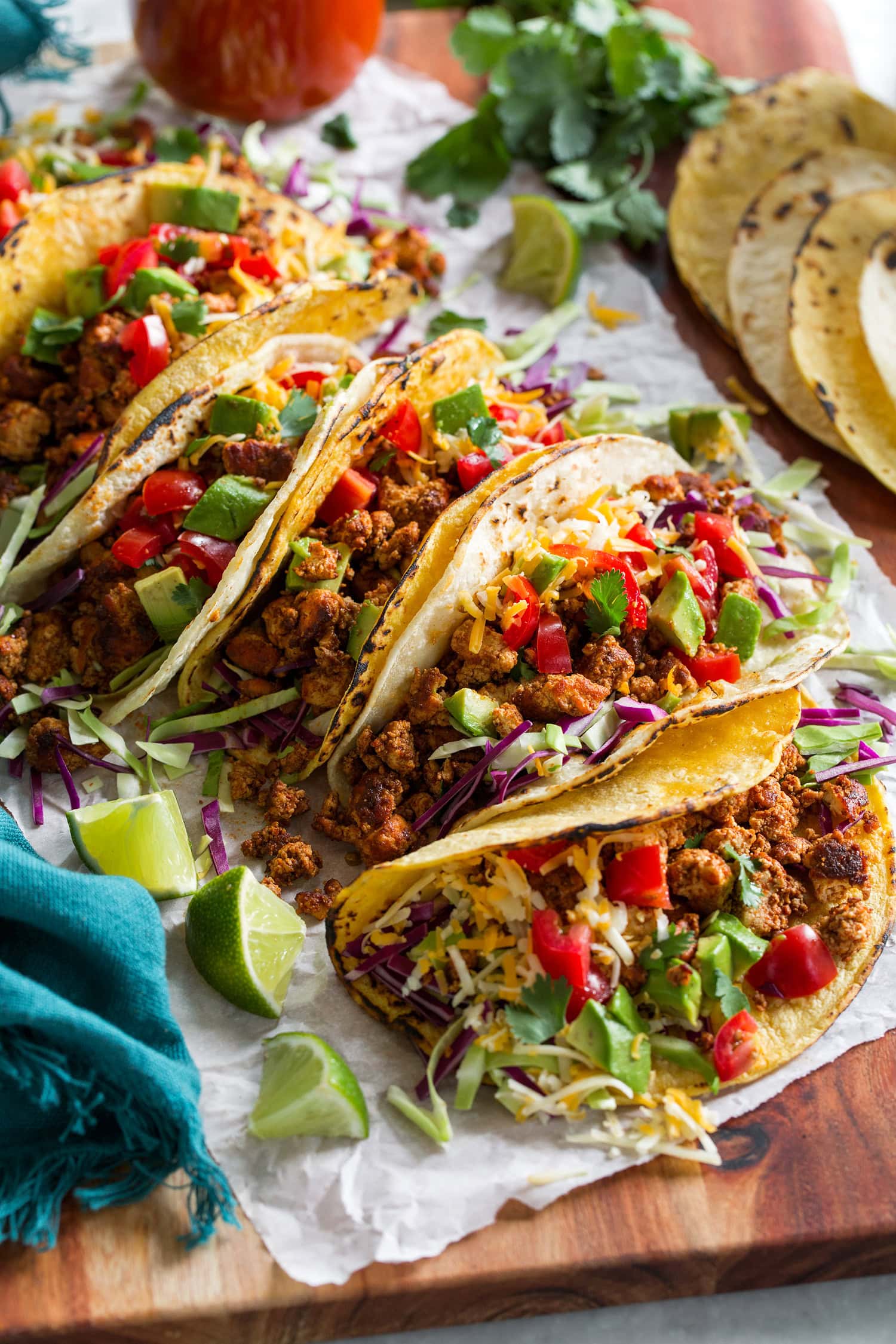 Row of ground tofu tacos shown from the side with lime wedges for serving.