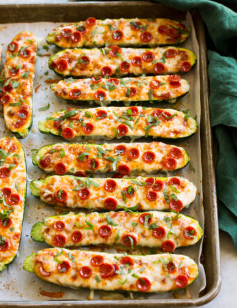 Zucchini Pizza Boats on a large baking sheet with a green cloth to the side.